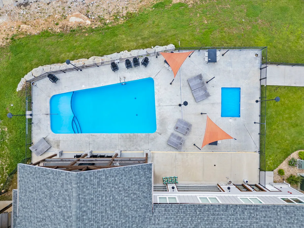 The image features an inviting outdoor swimming pool surrounded by sunshade structures, a seating area, and lush greenery. The scene is set up for relaxation and group activities, with plenty of space for sunbathing and social gatherings.