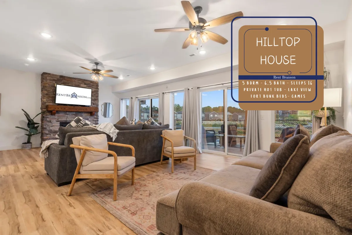 A cozy and inviting open-concept living room featuring a large sectional sofa, a stone fireplace with a TV mounted above, and expansive windows that flood the space with natural light. The arrangement is ideal for movie nights, board games, and enjoying sunset views.