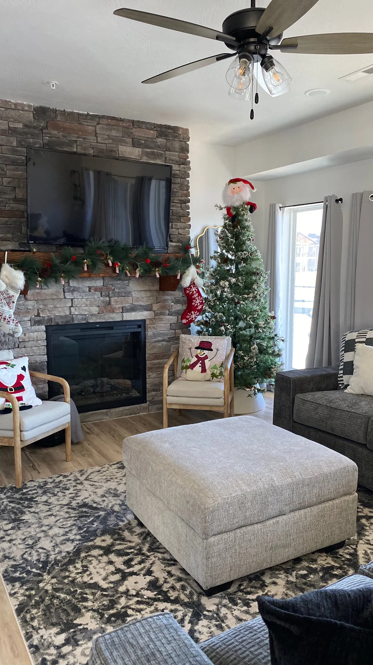 A cozy interior scene showcasing a stone fireplace, Christmas tree, and plush seating. The space is decorated for the holidays, with a warm, festive atmosphere perfect for winter relaxation and family gatherings.