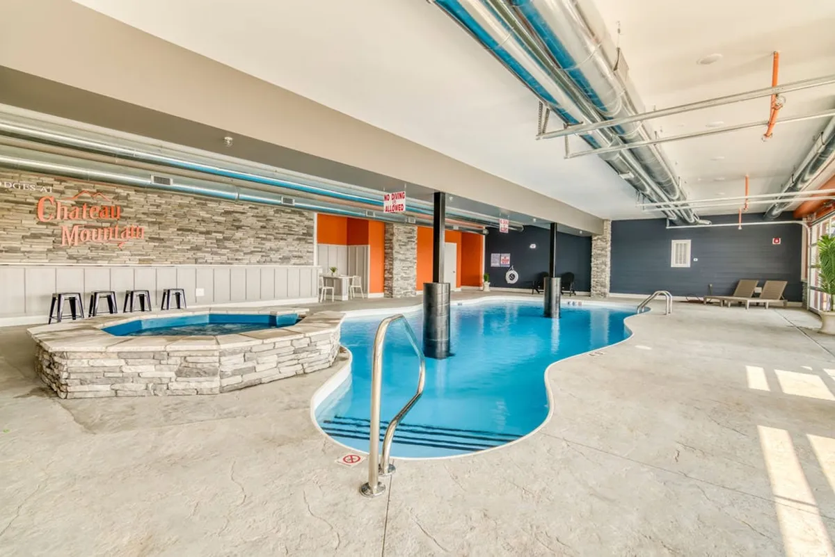 This image features an inviting indoor pool area complete with a hot tub and the Chateau Mountain sign, creating a tranquil and rejuvenating atmosphere. Guests are seen swimming, relaxing in the hot tub, and socializing, evoking the year-round enjoyment of the community's heated pool amenities.