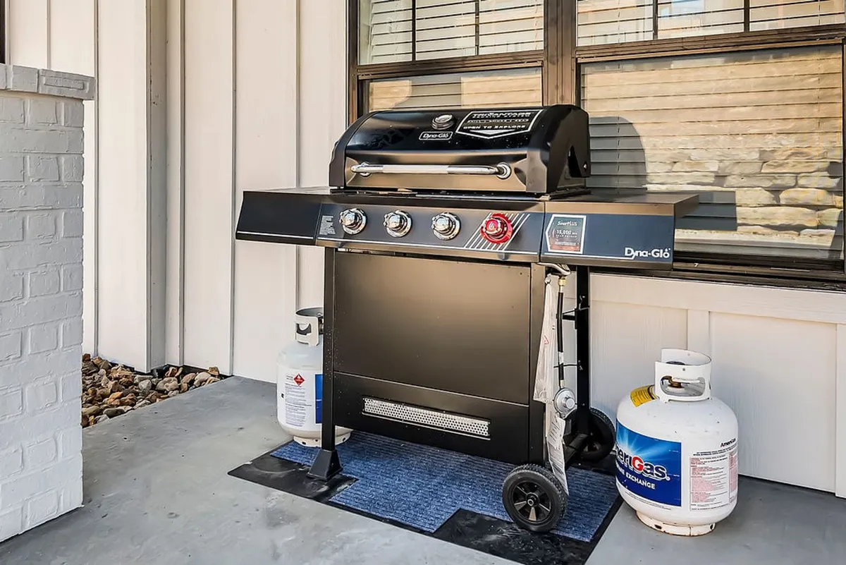 A close-up of a deck area featuring a grill, propane tanks, and a cozy rug, highlighting the functional space for barbecuing and outdoor dining. The setup suggests casual social gatherings and meals enjoyed in the fresh air.