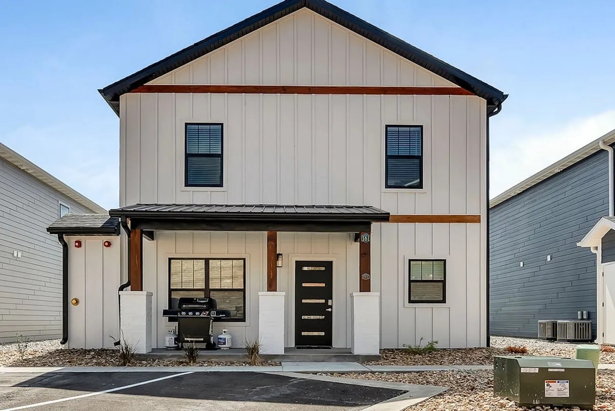 This image features the modern facade of Hilltop House, highlighting the front door, porch area, and an outdoor grill. The porch setting is inviting and hints at both relaxation and social activities. The scene is bathed in welcoming light, making it ideal for gatherings after a day out.