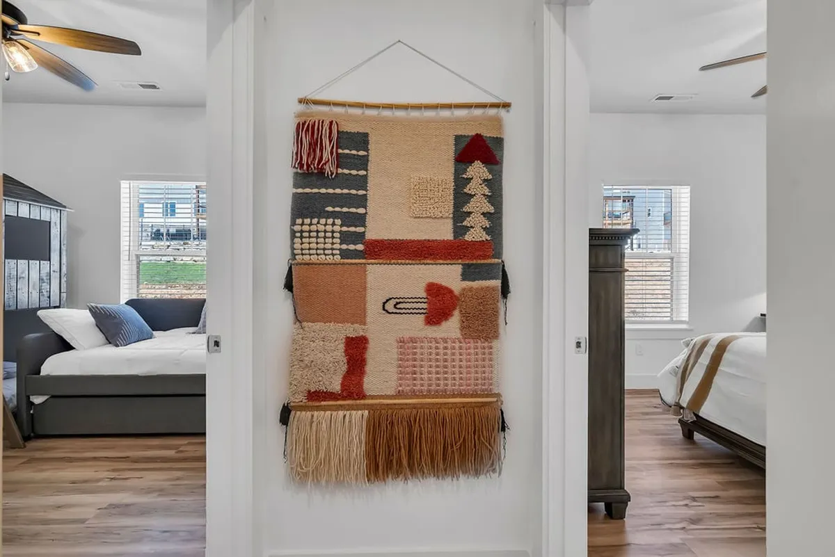 A bright, airy bedroom with a large window offering natural light, soft bedding, and a textile wall hanging. The space exudes comfort and relaxation, ideal for recharging after outdoor activities.