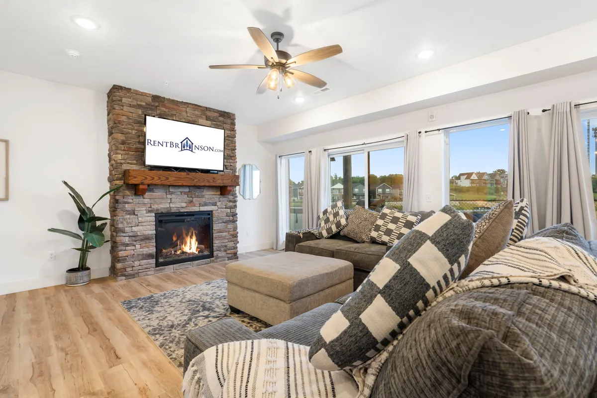 This interior scene centers on a fireplace surrounded by comfortable seating, large windows letting in natural light, and a flat-screen TV. The setting is perfect for cozy evenings, watching games, or relaxing with guests.