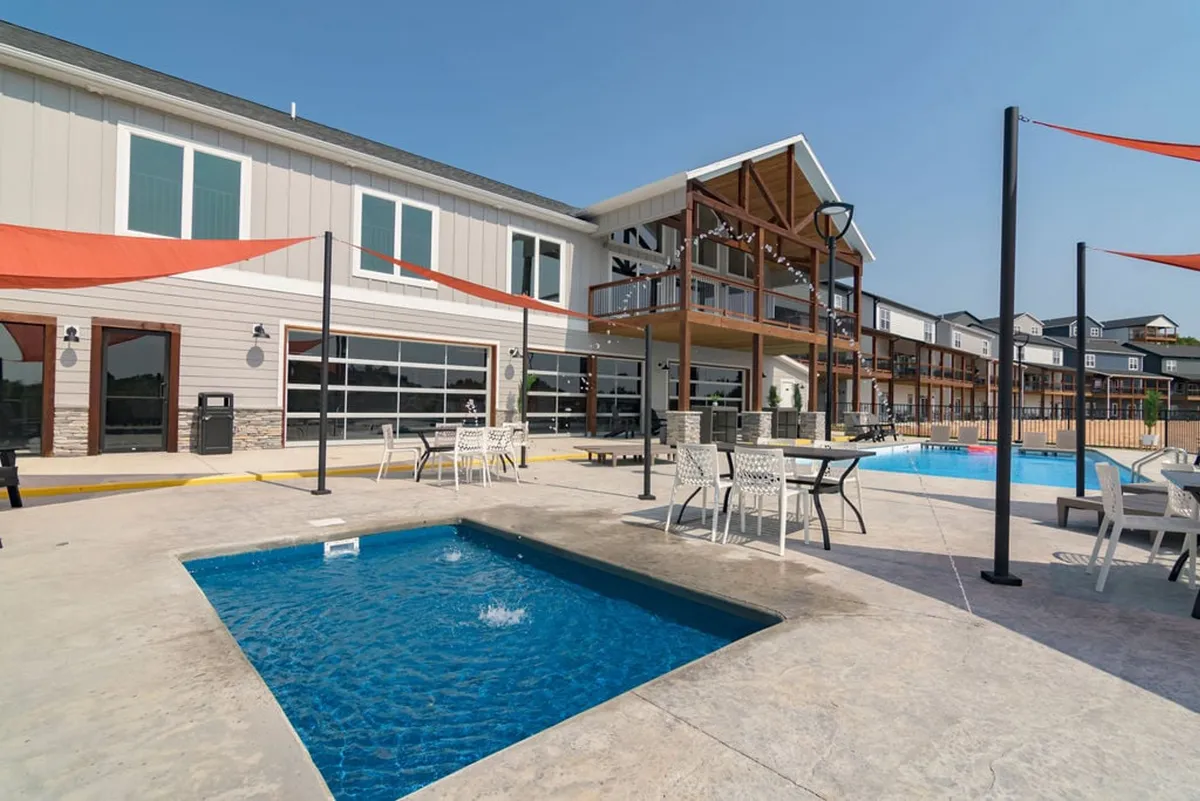 A spacious outdoor pool area is pictured, complete with a hot tub, outdoor seating, and the building’s facade in the background. The setting is lively yet relaxed, with ample space for swimming, sunbathing, and gathering with friends and family.